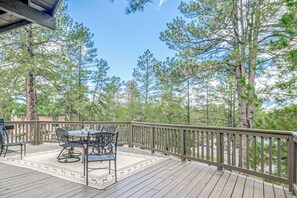 A wooden deck with outdoor furniture, surrounded by tall pine trees. - Comfortable Cabin w/ Hot Tub, Near Old Midtown (Ruidoso)