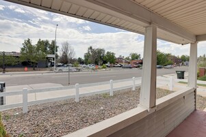Un espacio al aire libre techado con cerca blanca, camino pavimentado y automóviles estacionados.