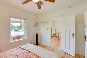 Un dormitorio con cama, ventilador de techo, ventana y puerta que da a otra habitación.
