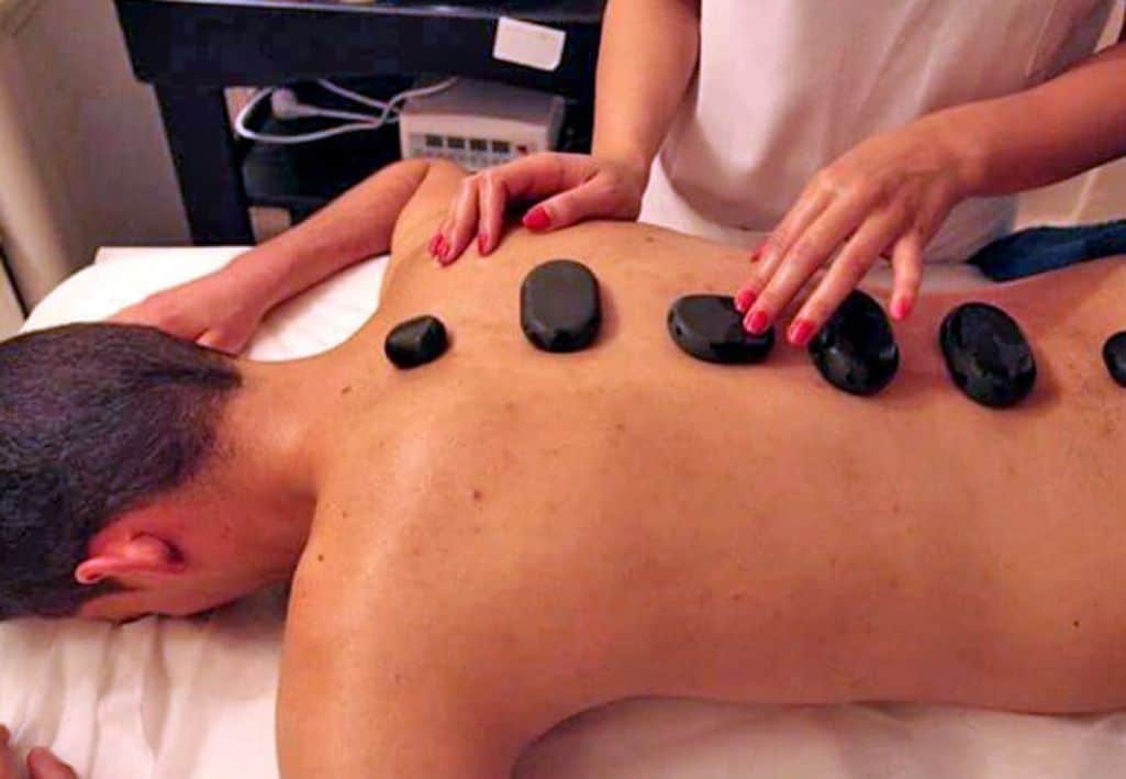 A person receiving a back massage with black stones placed on their back.
