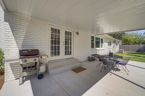 A covered patio with a barbecue grill, outdoor seating, and a white brick wall. - Charming Tulsa Home Near Lafortune Park (Tulsa)