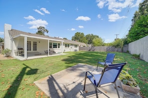 A residential backyard with a covered patio, two blue lawn chairs, and a wooden fence. - Charming Tulsa Home Near Lafortune Park (Tulsa)
