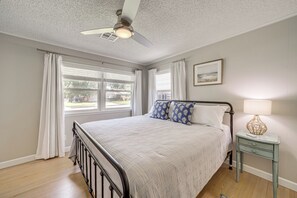 A bedroom with a bed, a nightstand, a lamp, a ceiling fan, and a window with curtains. - Charming Tulsa Home Near Lafortune Park (Tulsa)