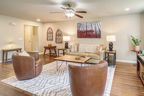 A living room with a ceiling fan, a painting of a forest, and a sofa with a throw blanket. - Private Workout Studio & Fenced Yard! Tulsa Escape (Tulsa)