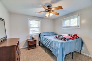 Quarto com cama, mesa de cabeceira, cômoda e ventilador de teto.