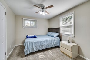 Ein Schlafzimmer mit einem Bett, einem Nachttisch, einem Deckenventilator und einem Fenster mit Jalousien.