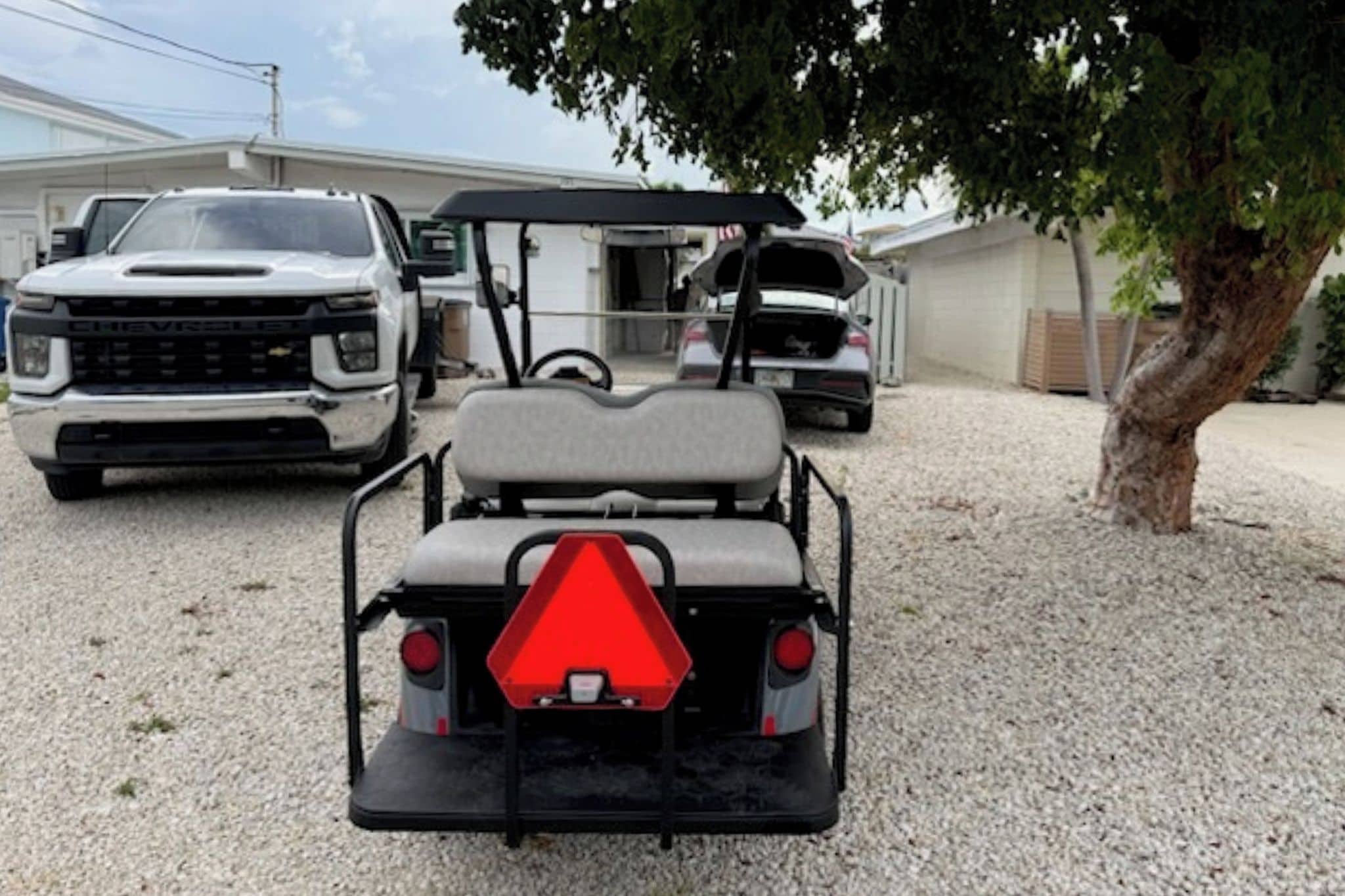 Un carrito de golf con una señal de advertencia triangular roja, estacionado sobre una superficie de grava.