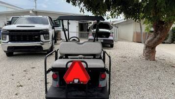 Un carrito de golf con una señal de advertencia triangular roja, estacionado sobre una superficie de grava.