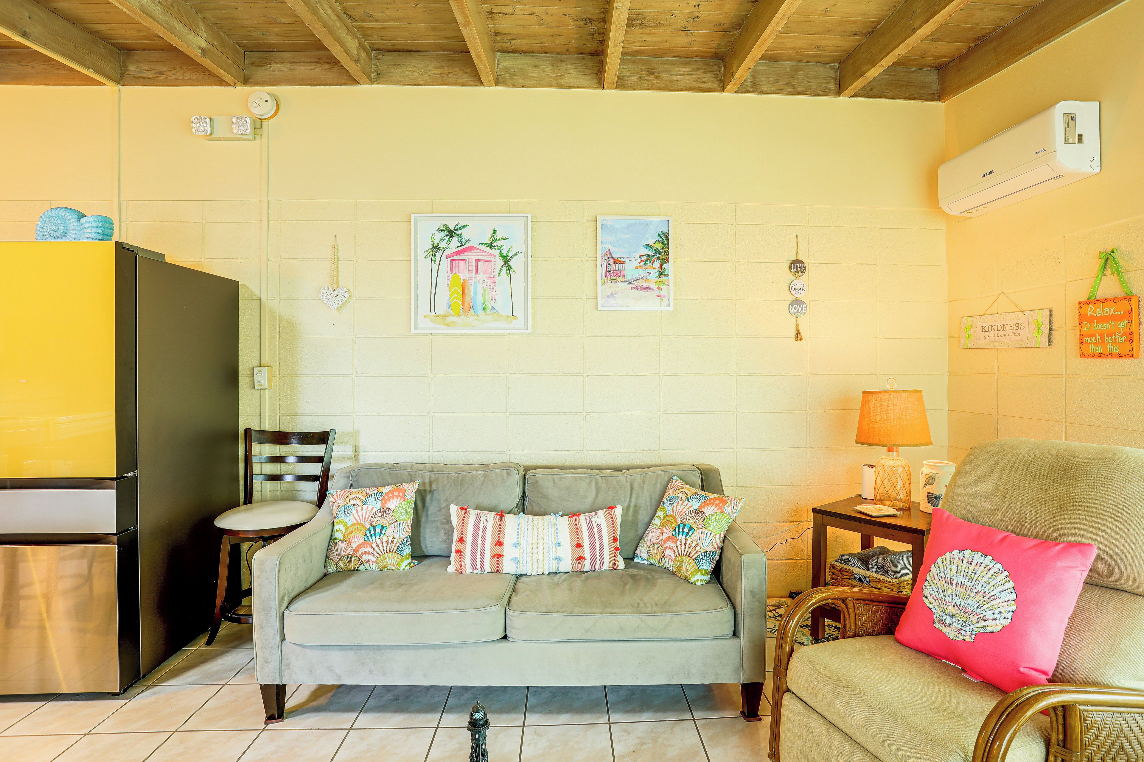 A living room with a sofa, a chair, a small table with a lamp, and a wall with framed pictures and wall decorations.