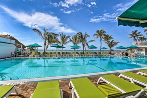 A pool area with clear blue water, green umbrellas, and lounge chairs.