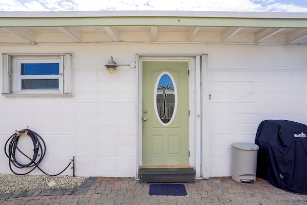A house with a green door, a window, a hose, and a barbecue grill.