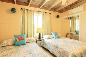 A bedroom with two beds, a window with curtains, a bedside lamp, and a mirror. - 1/2 Mi to Ocean! Canal-front Key Colony Beach Home (Key Colony Beach)
