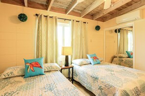 A bedroom with two beds, a window with curtains, a bedside lamp, and a mirror.