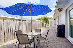 A patio with a round table and chairs, a blue umbrella, and a wooden fence.