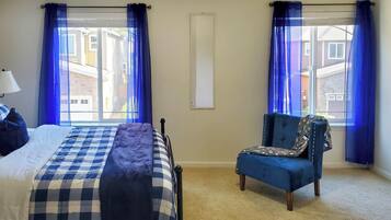A bedroom with a bed, a chair, and two windows with curtains.