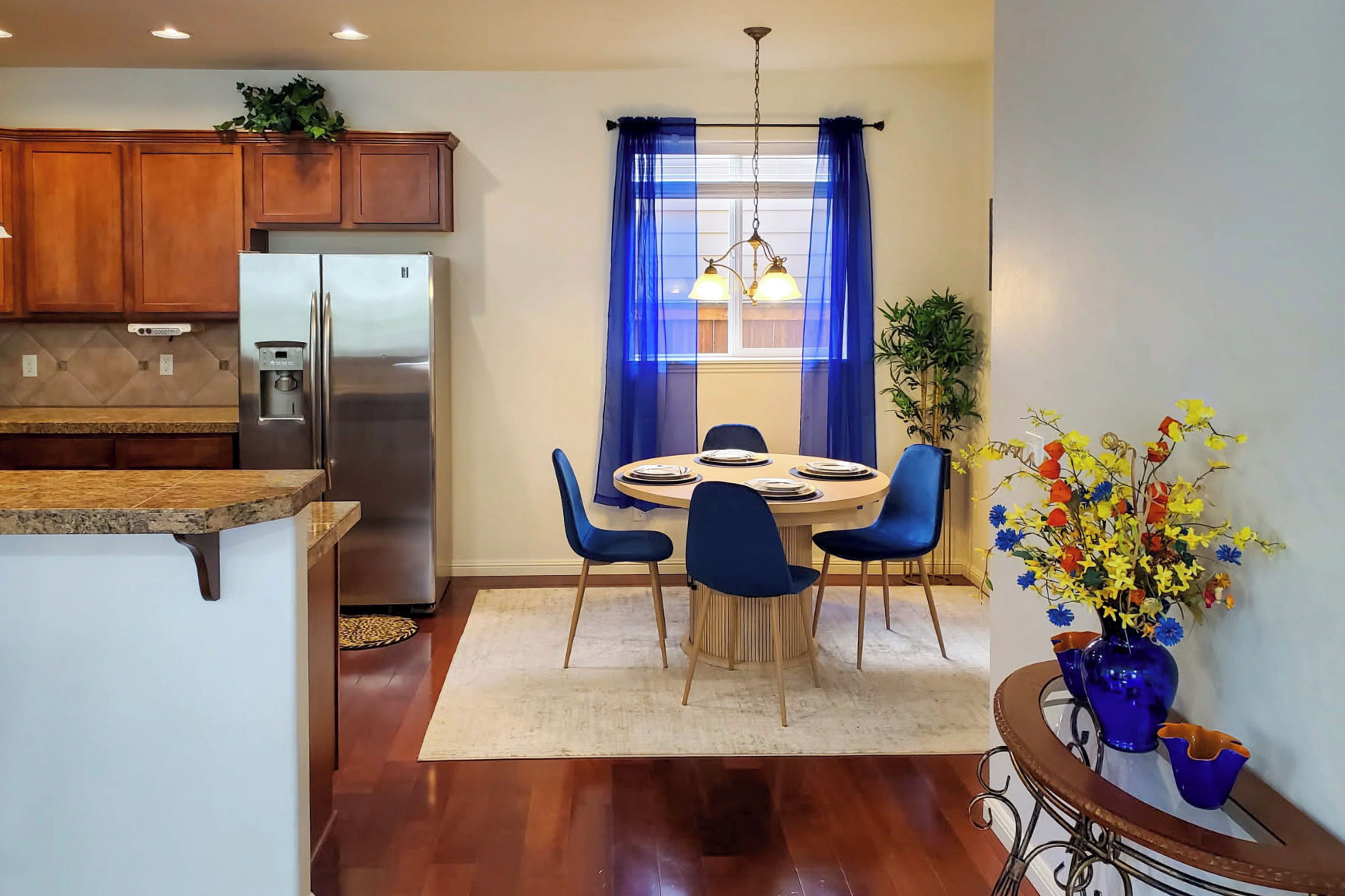 A modern kitchen with a built-in refrigerator, wooden cabinets, and a dining area with a round table and blue chairs.