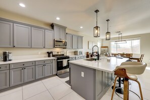 Cozinha moderna com armários cinza, ilha central, eletrodomésticos de aço inoxidável e iluminação pendente.