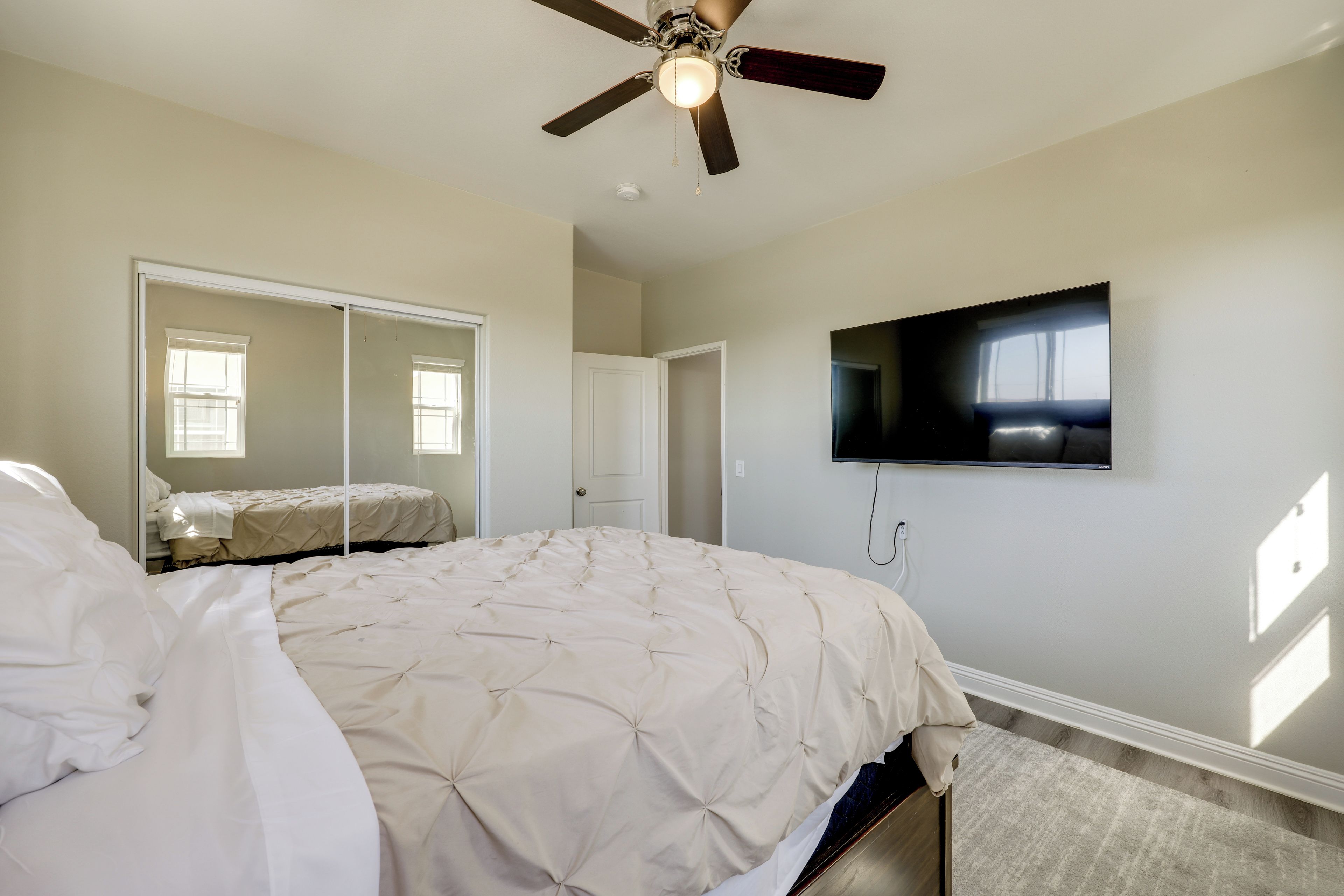 A bedroom with a bed, a ceiling fan, a television mounted on the wall, and a door.
