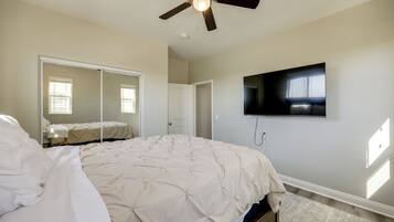 A bedroom with a bed, a ceiling fan, a television mounted on the wall, and a door.