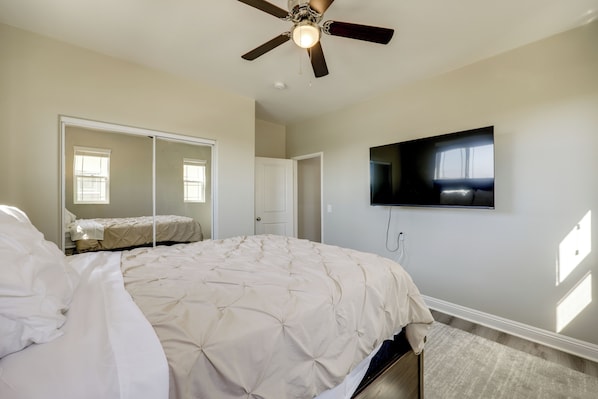 A bedroom with a bed, a ceiling fan, a television mounted on the wall, and a door.