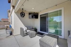 A covered patio with wicker furniture, a flat-screen TV, and a sliding glass door.
