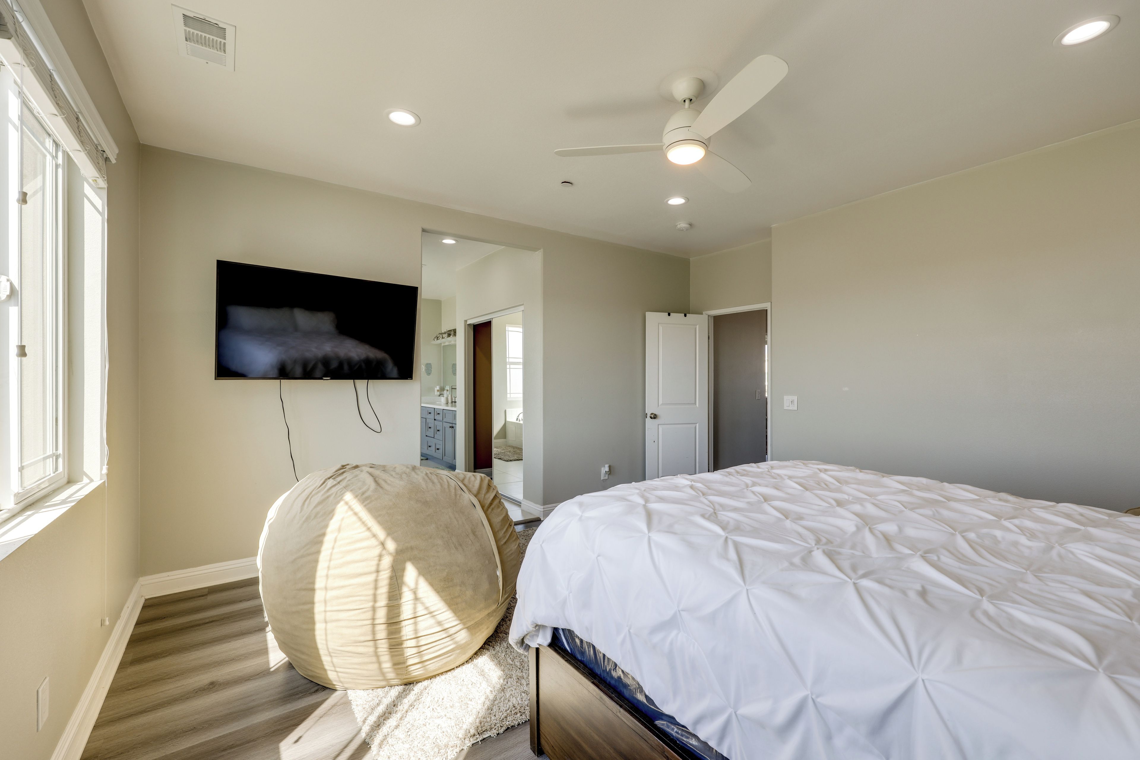 Une chambre à coucher avec un lit, un ventilateur de plafond, un téléviseur fixé au mur et une fenêtre.