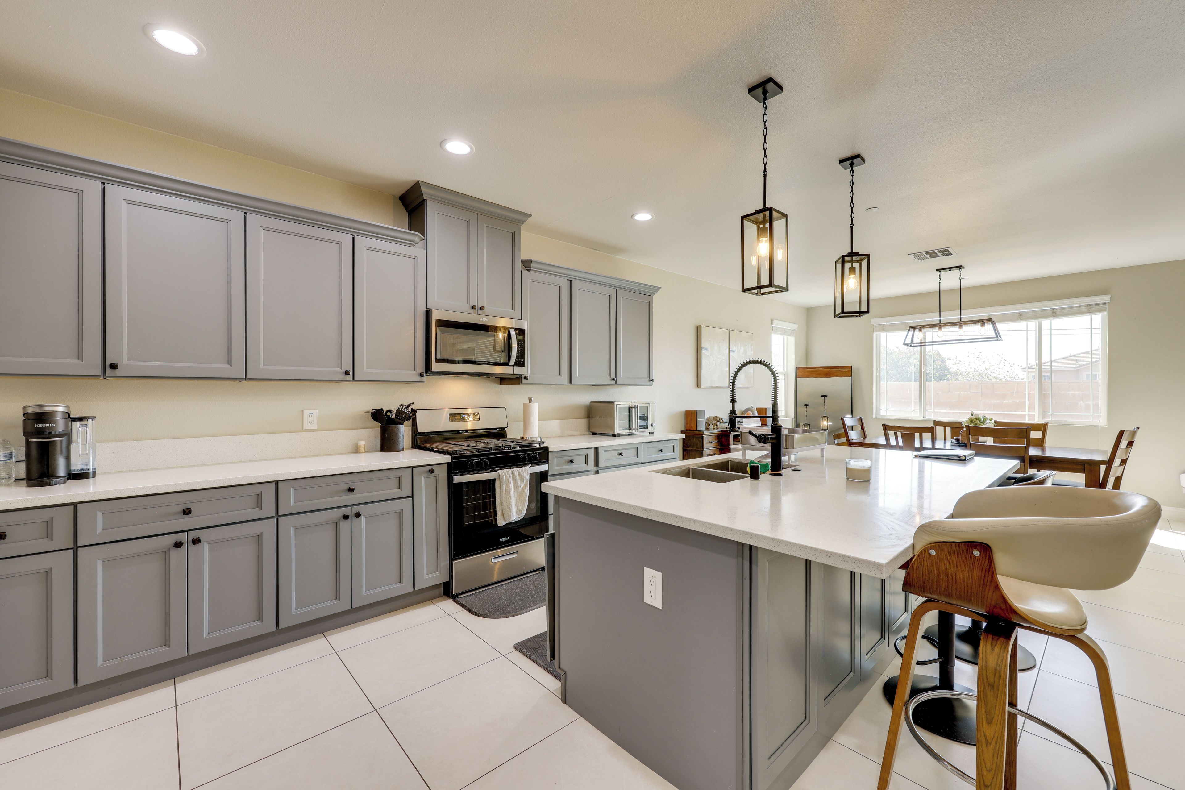A modern kitchen with grey cabinets, a central island, stainless steel appliances, and pendant lighting.