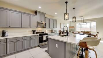 A modern kitchen with grey cabinets, a central island, stainless steel appliances, and pendant lighting.