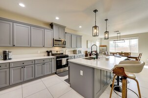 A modern kitchen with grey cabinets, a central island, stainless steel appliances, and pendant lighting.