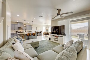 Una sala de estar moderna con un sofá seccional grande, un comedor con barra y una cocina con armarios grises.