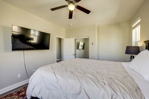 Un dormitorio con una cama grande, un ventilador de techo, un televisor de pantalla plana montado en la pared y una puerta que da a otra habitación.