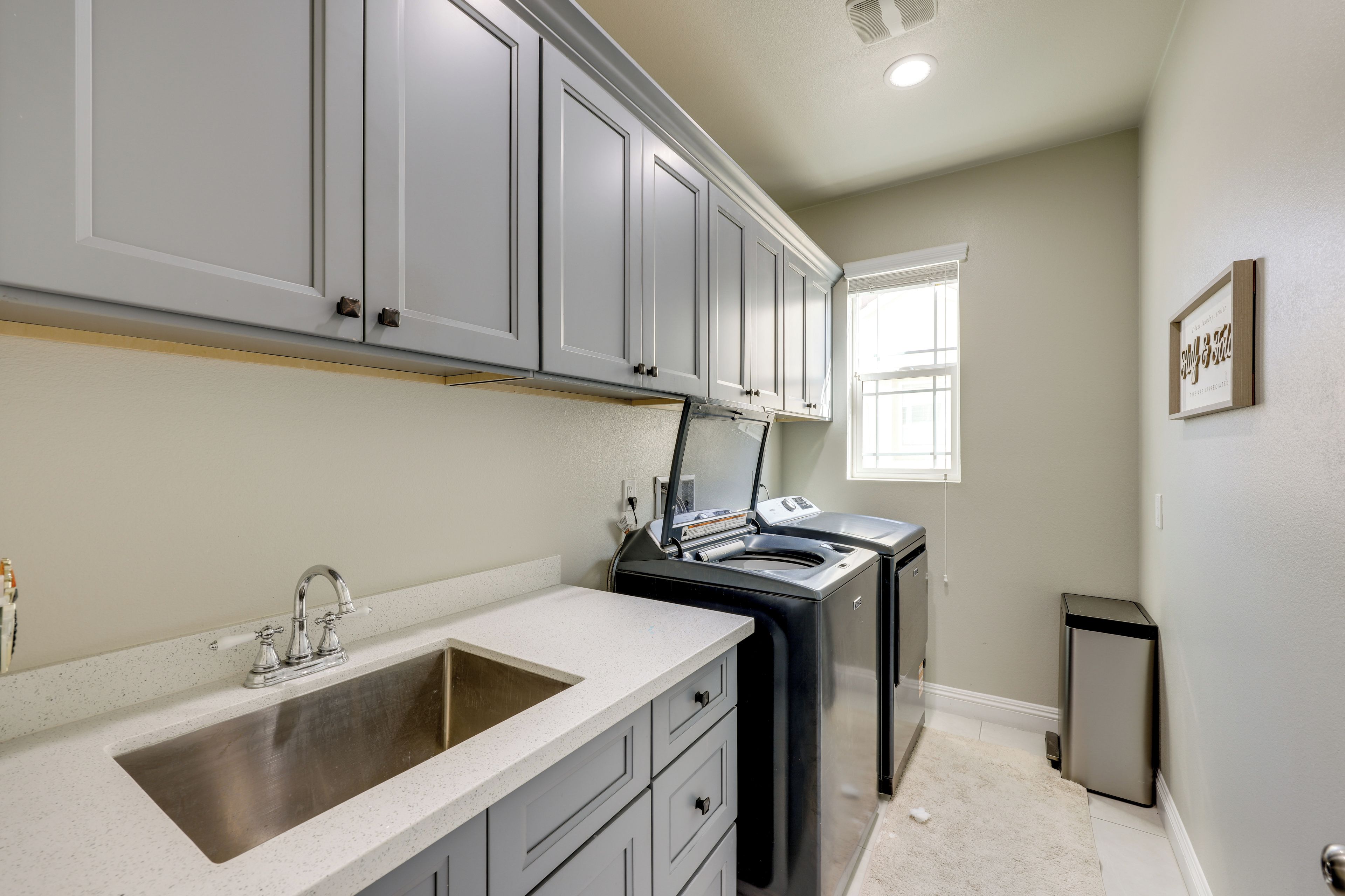 A kitchen with grey cabinets, a stainless steel sink, a built-in oven, and a small trash bin.