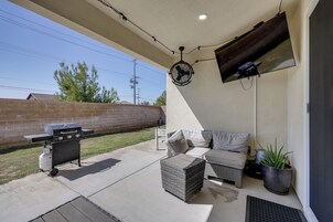 Un patio techado con una parrilla, muebles de exterior, un ventilador y un televisor montado en la pared.