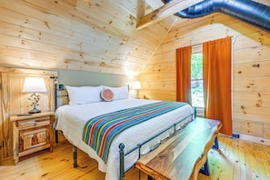 Ein Zimmer in einer Holzhütte mit einem Bett, Nachttischen und einem Fenster mit Vorhängen.