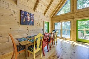 Un interior de madera con una mesa de comedor, sillas coloridas y ventanas amplias.