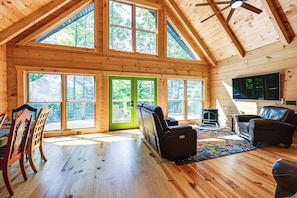 Ein Blockhaus-Interieur mit hohen Decken, großen Fenstern, einem Kamin und Ledersitzmöbeln.