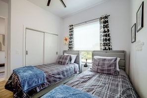 A bedroom with two beds, a window with curtains, a door, and a wall with a framed picture. - Community Boat Ramp! Family Escape w/ Fenced Yard (Granbury)