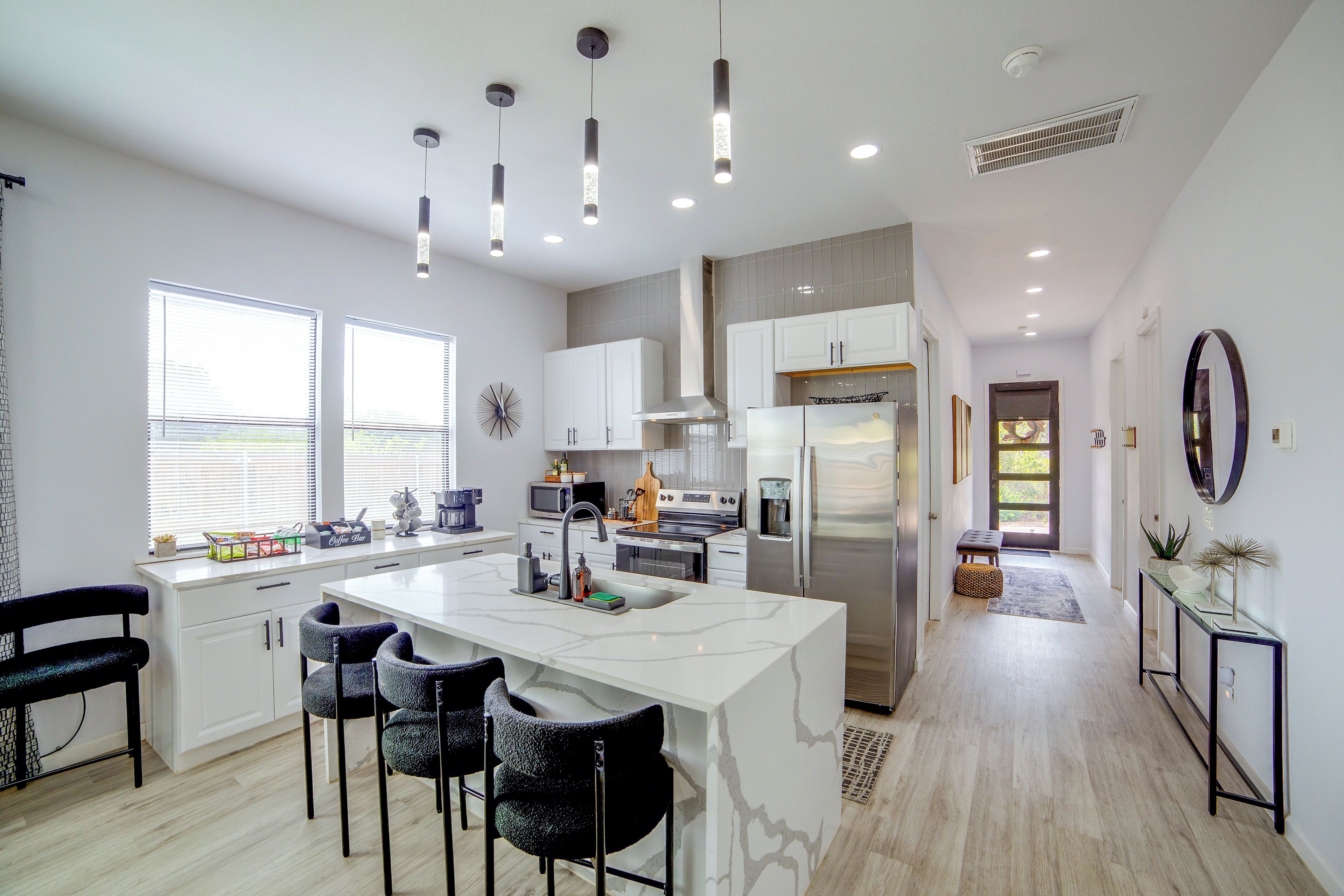 A modern kitchen with a central island, bar stools, a refrigerator, and a microwave.