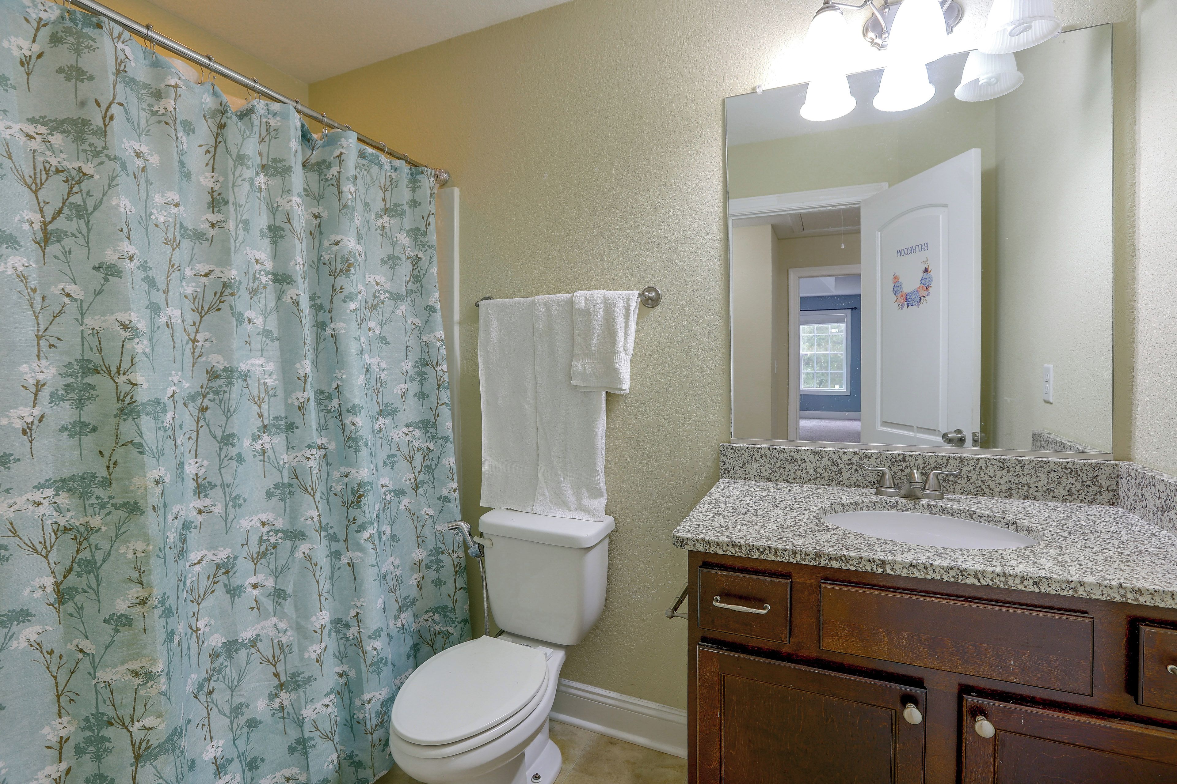 A bathroom with a toilet, a shower curtain with a floral pattern, a vanity with a sink, and a mirror.