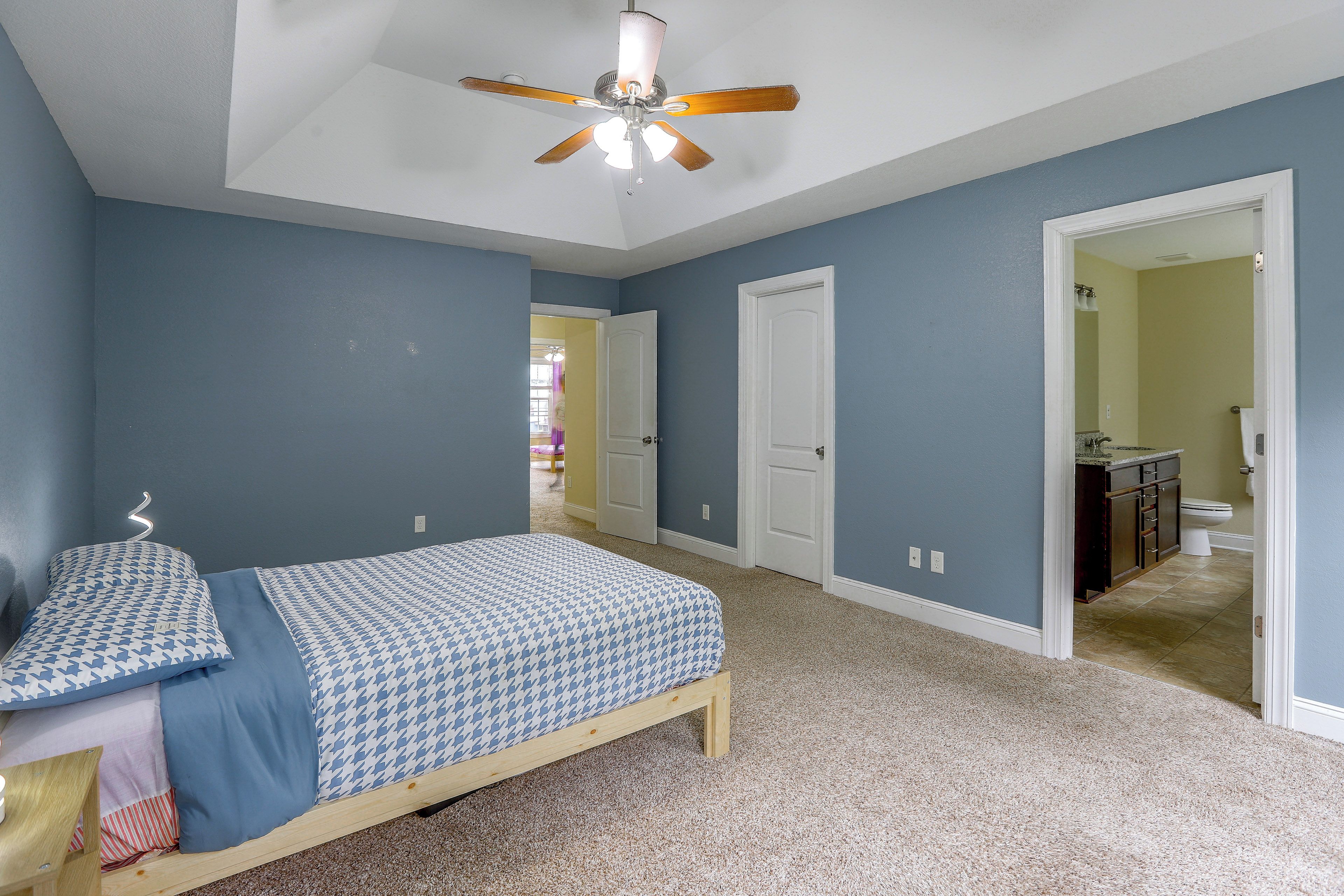 Un dormitorio con cama, ventilador de techo y puerta que da a un baño.