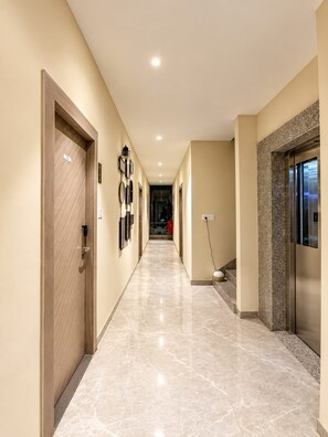 A hotel corridor with a marble floor, wooden doors, and a modern elevator. - Hotel Saranga - Indore (Indore)