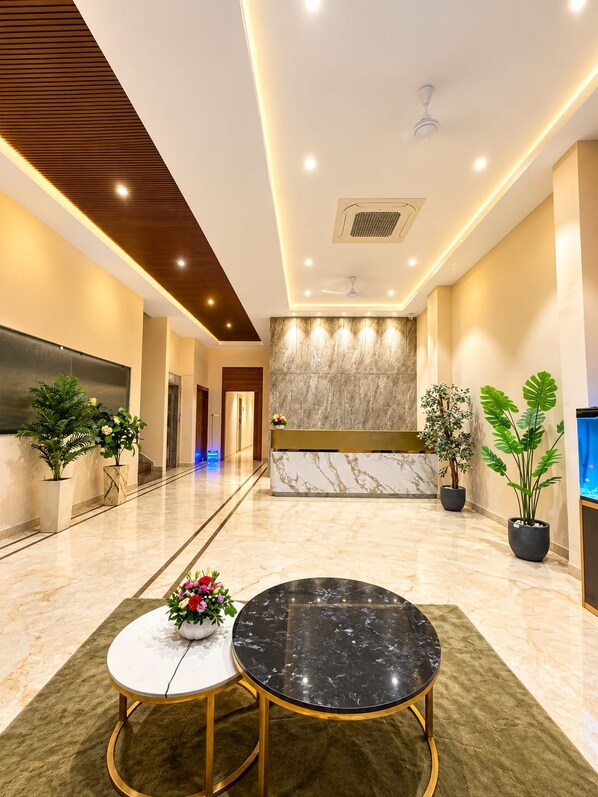 A hotel lobby with a reception desk, marble flooring, potted plants, and a large screen. - Hotel Saranga - Indore (Indore)