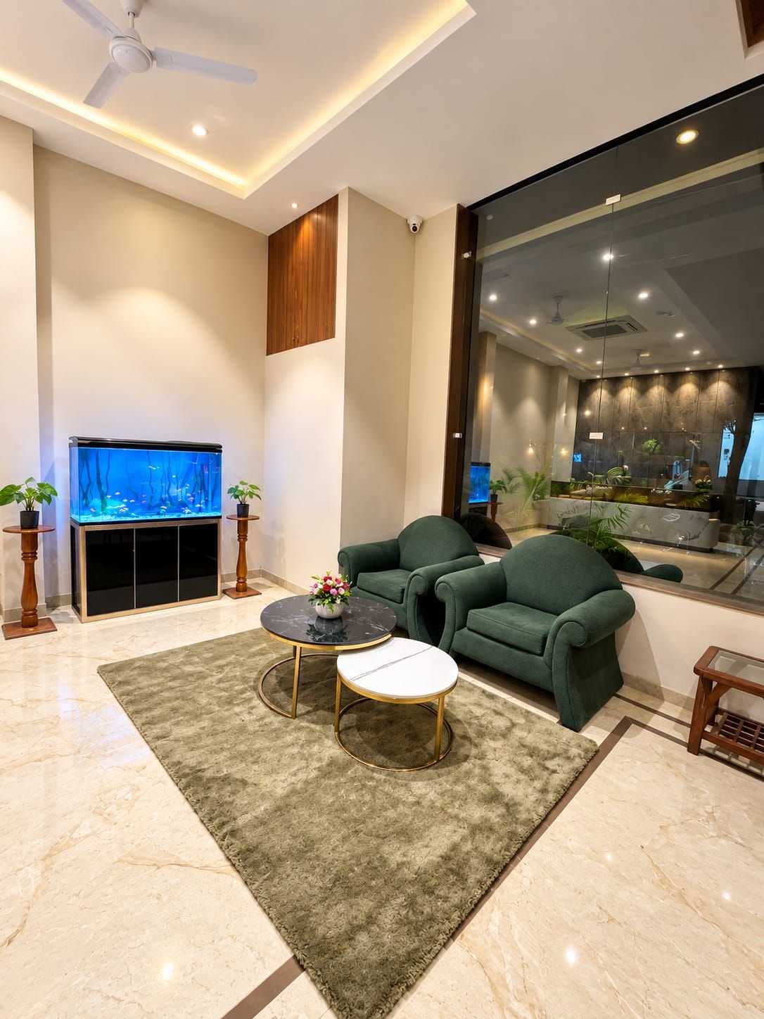 A modern living room with a flat-screen TV, green sofas, a marble coffee table, and a large aquarium.