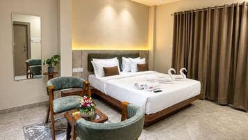 A hotel room with a bed, two chairs, a table with a vase, a ceiling fan, and a large window with curtains.