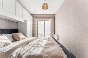 Ein modernes Schlafzimmer mit einem großen Bett, einem Kopfteil, einem Nachttisch und einem Fenster mit Vorhängen.