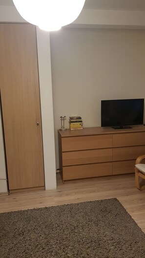 Ett rum med en garderob i trä, en tv på ett träställ och en liten hög med böcker.