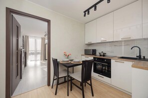 Une cuisine moderne avec des meubles blancs, un plan de travail noir et un coin repas comprenant deux chaises et une table dressée pour deux personnes.