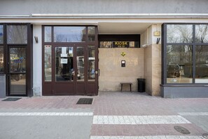 A building entrance with a brown door, a sign reading 'KIOSK KOD 129', and a small bench outside. - Warsaw | Przechodnia 2 | Bright Apartment | City View (Warszawa)