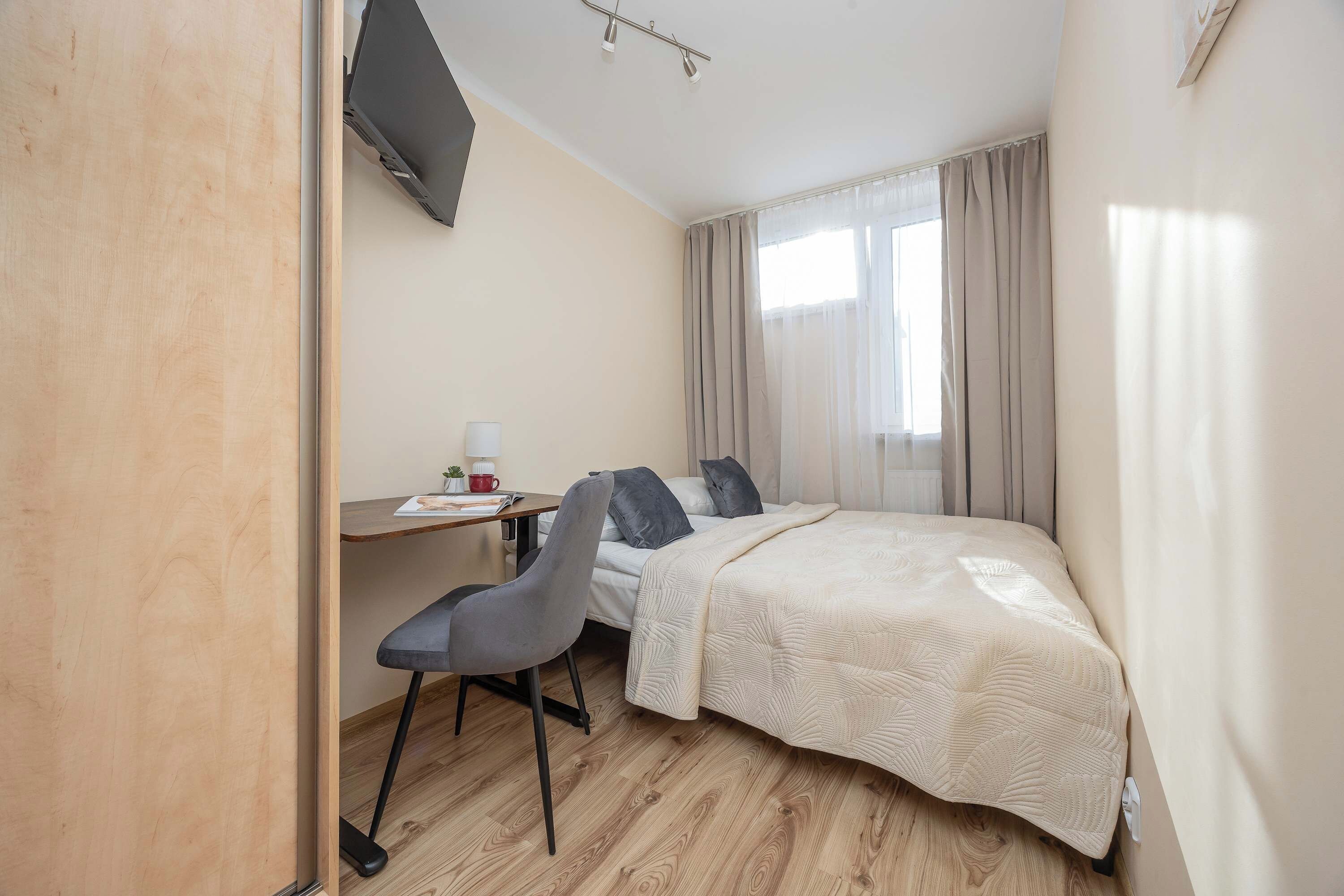 A hotel room with a bed, a desk, a chair, a lamp, and a window with curtains.