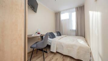 A hotel room with a bed, a desk, a chair, a lamp, and a window with curtains.